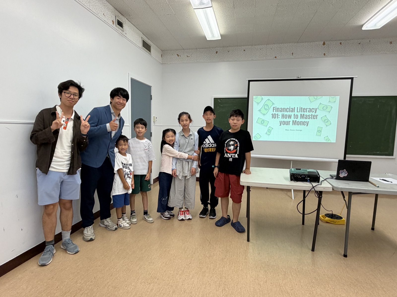 George and a co-presenter standing with a group of kids in front of a projected slide titled Financial Literacy 101: How to Master your Money.